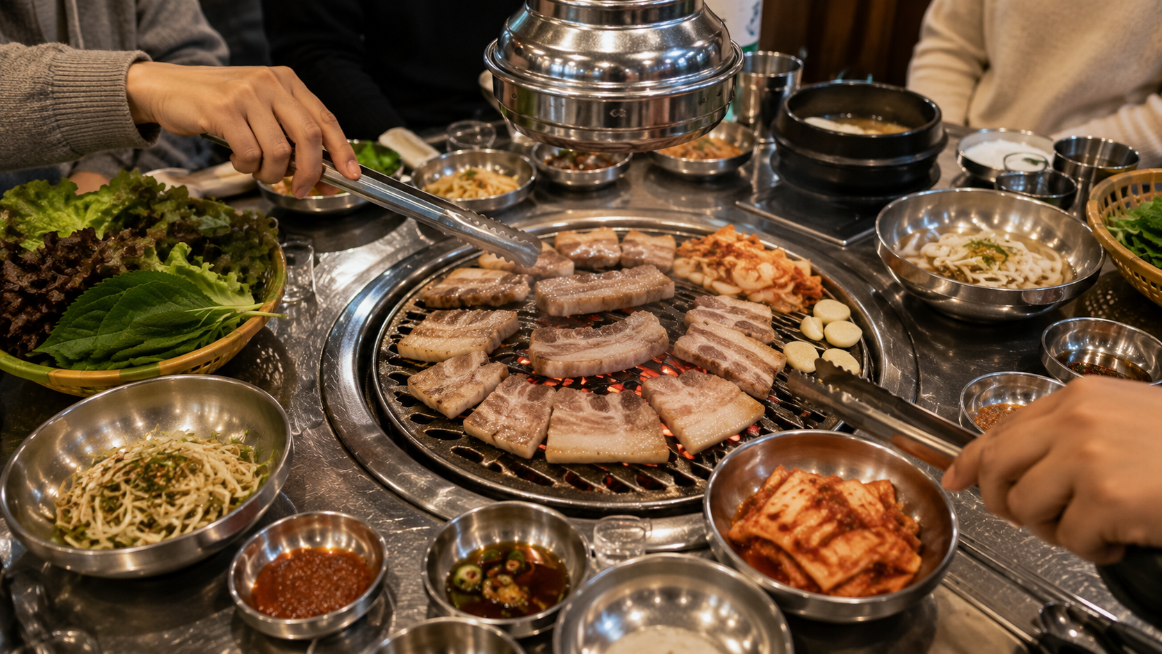 A Korean barbecue table in Seoul with pork belly cooking on a built-in grill, surrounded by lettuce, kimchi, sauces, and