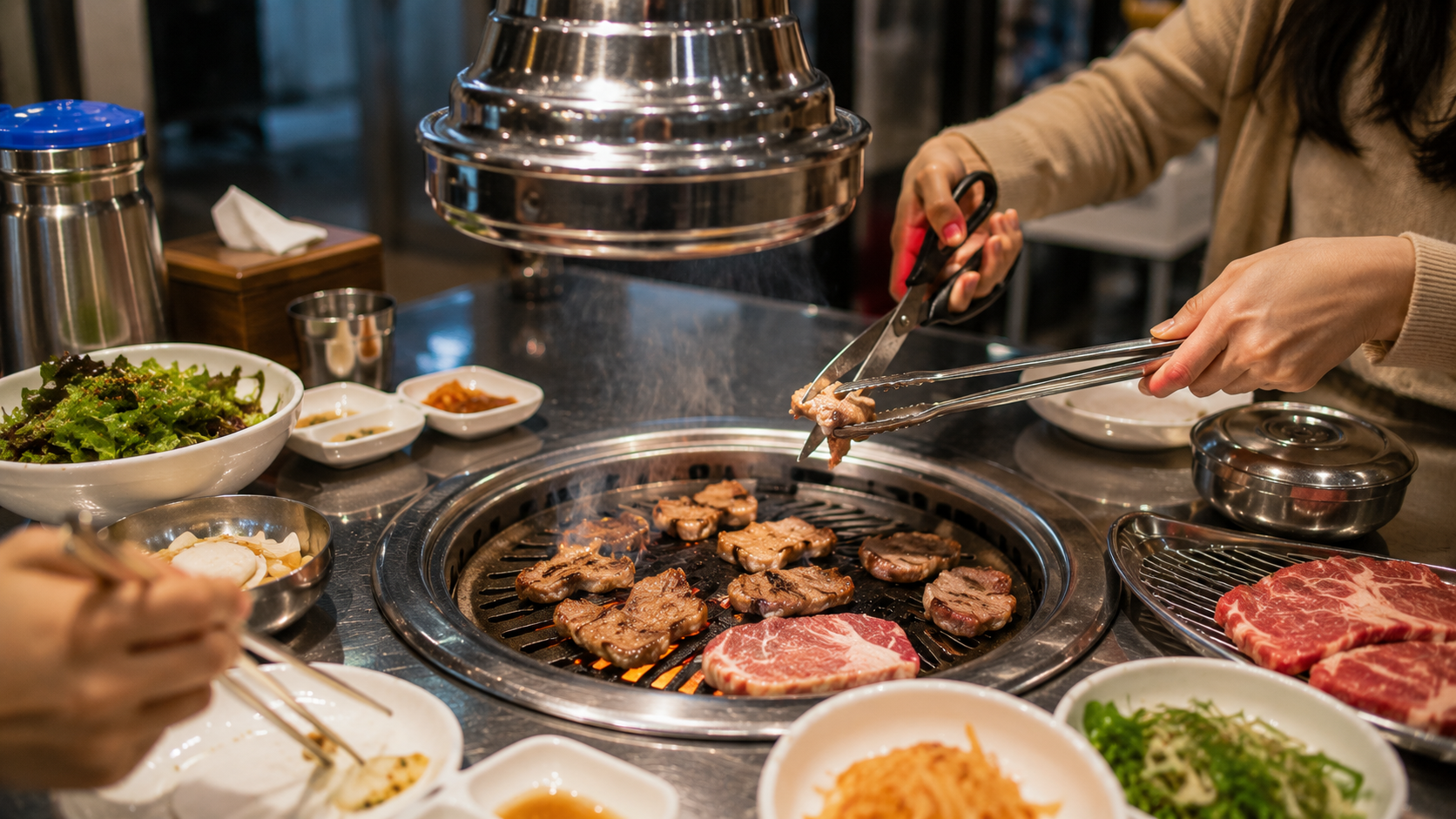 Diners at a Korean barbecue restaurant using tongs and scissors at a tabletop grill