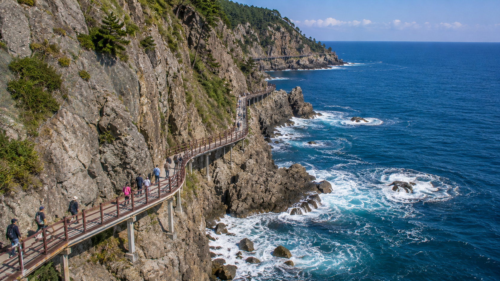 Travelers walking the Badabuchae Trail beneath rugged cliffs with waves breaking below