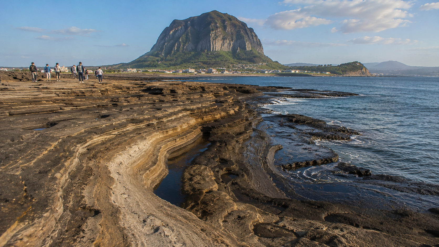 The layered rock shoreline of Yongmeori Coast with Sanbangsan in the background
