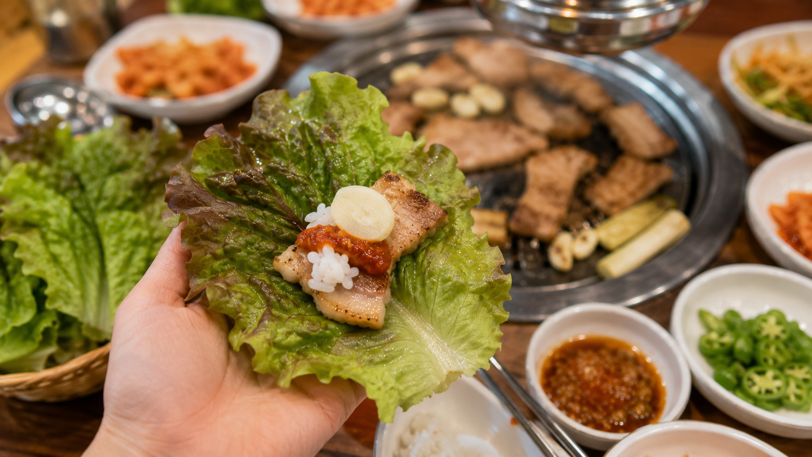 Close-up of a diner's hand assembling a lettuce wrap with grilled pork, rice, garlic, and ssamjang in a Korean restauran